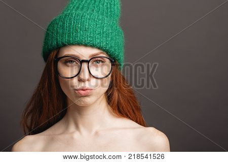 naked ginger woman wearing circle glasses and green hat pouting her lips ready for kiss