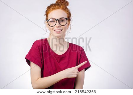 Portrait of redhead girl with perfect freckled skin pointink sideway, looking at camera and showing somewhere