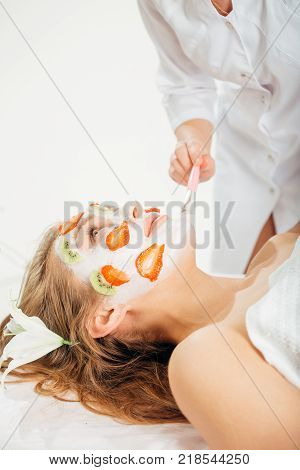 Beautiful young woman receiving fruit mask on a face in beauty salon - indoors.