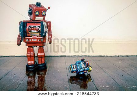 Big retro robot toy humiliates little robot on a wooden floor with reflection