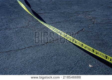Caution tape in spanish. Yellow tape marked caution in English and cuidado in Spanish on black asphalt.