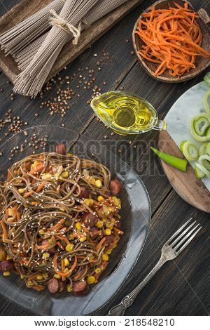 Soba noodles with sousages, leek, corn and korean carrot on a dark wooden rustic background top view