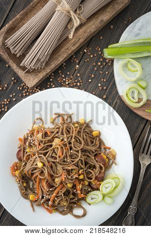 Soba noodles with sousages, leek, corn and korean carrot on a dark wooden rustic background top view