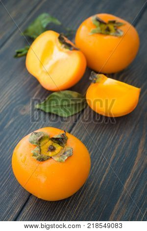 Sliced ripe persimmons with green leaves on dark rustic wooden background closeup