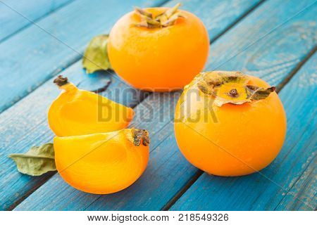 Sweet orange persimmons with green leaves on blue rustic wooden table closeup