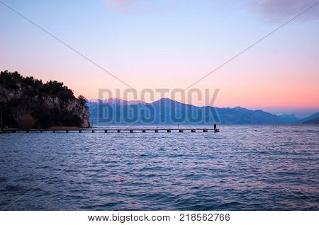 Romantic violet sunset on a lake with a long pier and people walking on it
