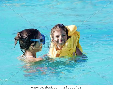 Brother and sister playing in the swimming pool at the day time. People having fun outdoors. Concept of happy family.