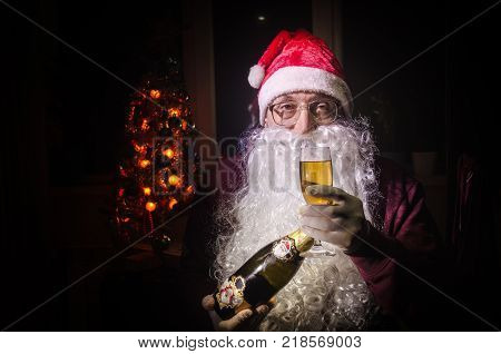 Santa Claus toasting with a glass of champagne (Bottle) Santa Claus with a glass of champagne celebrating and smiling. Selective focus dark toned background