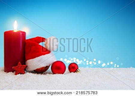 Avent candle and christmas decoration isolated on blue background. Christmas background with snow, candle and Santa Claus hat.