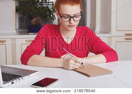 Attractive Female Student With Ginger Hair Bun Thinks About Coursework Strategy, Works With Laptop C