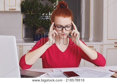 Attractive Female Student With Ginger Hair Bun Thinks About Coursework Strategy, Works With Laptop C