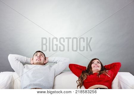 Happy smiling young couple relaxing on couch at home. Calm carefree man and woman resting with arms behind head. Healthy relationship.