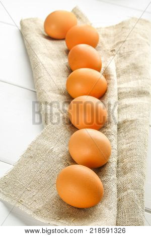 Raw brown chicken eggs in one row on burlap on a white wooden table. Ingredients for cooking