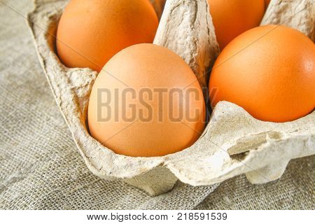 Raw brown chicken eggs in a cardboard tray with cells on sacking on a white wooden table. Ingredients for cooking