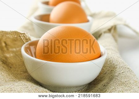 Raw brown chicken eggs in glass bowls on a white wooden table. Ingredients for cooking