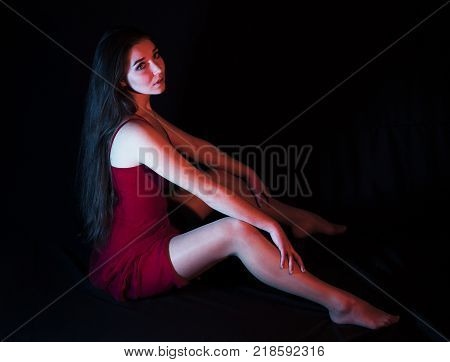 Beautiful Sexy Girl in red dress sitting on the floor with Frenkly wide opened legs, studio shot