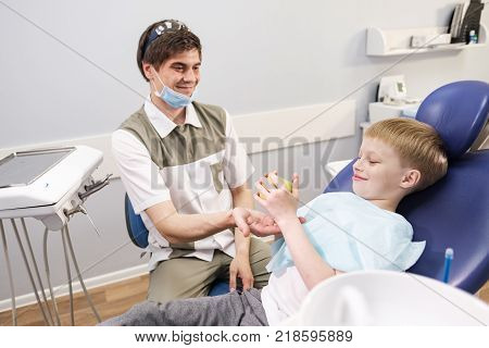 Doctor male dentist giving green apple to patient boy in dental chair