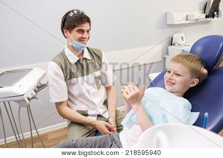 Doctor male dentist giving green apple to patient boy in dental chair
