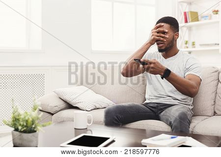 Young man wathing tv at home. Thrilled guy pointing with remote controller on tv-set, copy space