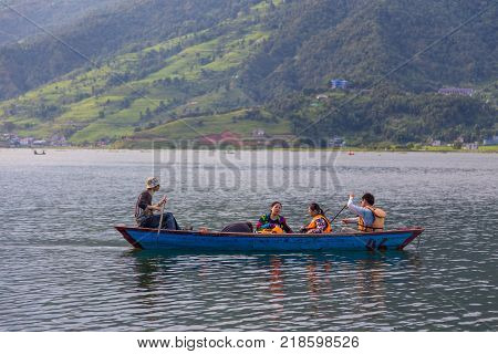 POKHARA NEPAL - September 29 2013: Tourists on old small boat sailing on the Phewa lake. Rowboat symbol of Phewa lakeside in Pokhara city.