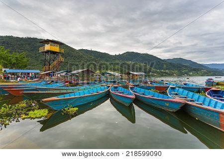 POKHARA NEPAL - September 29 2013: Tourist and old small boats on the Phewa lake. Rowboat symbol of Phewa lakeside in Pokhara city.