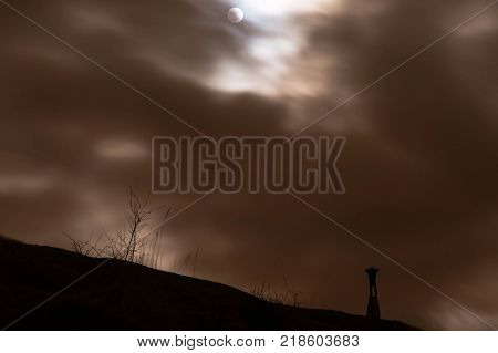 Silhouetted man looking at super moon through binoculars. Person observes large moon whilst standing on Trig Point on Solsbury Hill