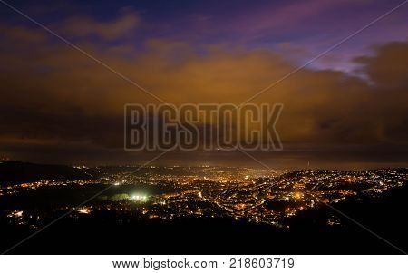 View of Bath at night from Solsbury Hill. The UNESCO World Heritage city seen nestling among hills from a high viewpoint under low clouds
