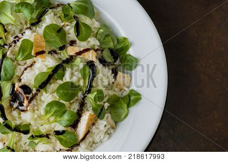 chicken and rice with valeriana salad and balsamic vinegar in a plate on wooden table
