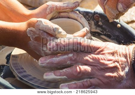 adult hand fed baby's hands to work with a potter's wheel, close up