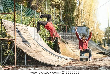 Urban athlete breakdancer performing somersault jump flip at skate park - Afroamerican guy watching friend acrobat dancing with extreme flipping move - Breakdance acrobatic and friendship concept