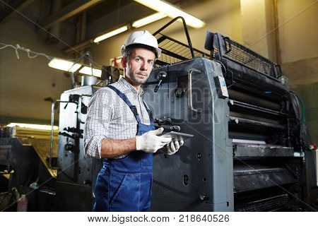 Young worker in uniform, gloves and helmet searching for online advice how to repair industrial machines