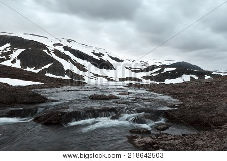 Typical norwegian landscape with snowy mountains and clear river near the famous Aurlandsvegen (Bjorgavegen), mountain road, Aurland, Norway.