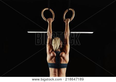 Full length rearview shot of a female athlete performing pull-ups on gymnastic rings. Fitness woman with strong beautiful body exercising on gym rings health power endurance competitive
