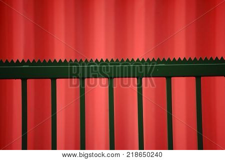 The side view of a orange Cargo Containers with a striking pointed-jagged green fence in front of it.