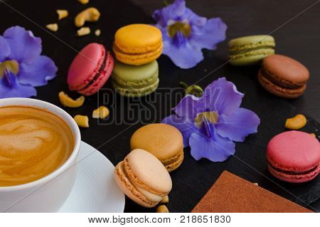Makarons with a cup of your favorite coffee and blue flowers on a black stone background. It's really amazing morning.