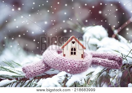 Christmas Toy house is wrapped in a warm scarf it's snowing.on a natural natural background of a real fir in the snow toned. Concept of winter Christmas new year warm cozy loving protecting the house. We prepare the house for the cold.