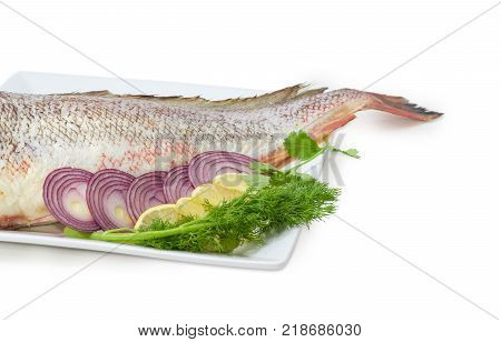 Fragment of the large square dish with uncooked red cod sliced lemon and red onion twigs of the dill and cilantro at shallow depth of field on a white background
