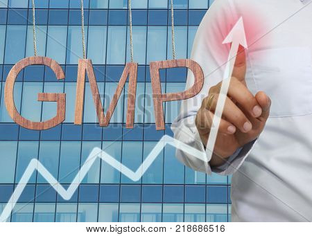 Wooden GMP text Stands for Good Manufacturing Practice hanging on rope and businessman point to the top of the graph on Skyscraper background.