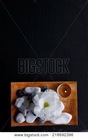 Wooden rectangular board with multiform pebbles for spa treatments On a black background. View from above.