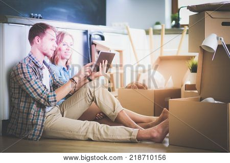 Young couple moving in new home.Sitting and relaxing after unpacking.Looking something on laptop. Young couple