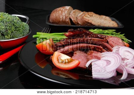 business lunch fresh roast beef meat slices on black plate wotj cutlery asparagus boiled broccoli rye bun on wooden table