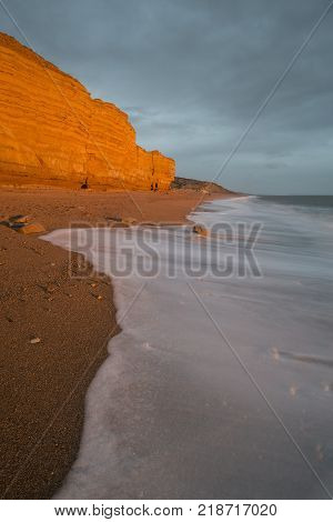Beautiful Vibrant Sunset Landscape Image Of Burton Bradstock Golden Cliffs In Dorest England