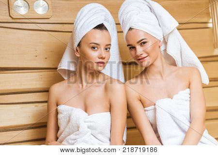 beautiful young women covered with towels relxing in sauna and looking at camera