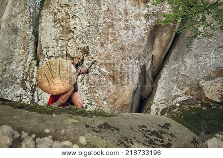Low angle full length shot of an armored Spartan soldier covering himself with a shield from enemies archers copyspace war fight conflict protection defensive safety bravery masculinity weapon.