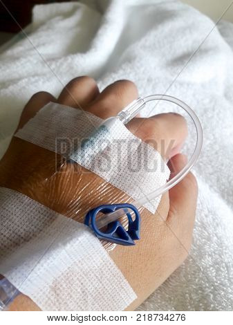 Patient hand with the tube of normal saline infusion on white cloth background