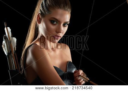 Close up studio portrait of a beautiful young female archer looking to the camera posing on black background seductively sexy sexuality femininity beauty archery fighter warrior weapon cosplay.