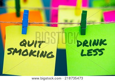 A set of colorful sticky notes with positive affirmation words and phrases hung from a clothesline by clothespins; featuring Quit Smoking and Drink Less.