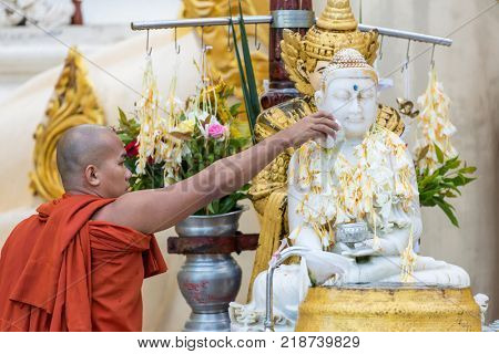 Yangon, Myanmar - September 27, 2016: Burmese buddhist monk pouring water over the Buddha statue for blessing in Shwedagon pagoda in Yangon, Myanmar