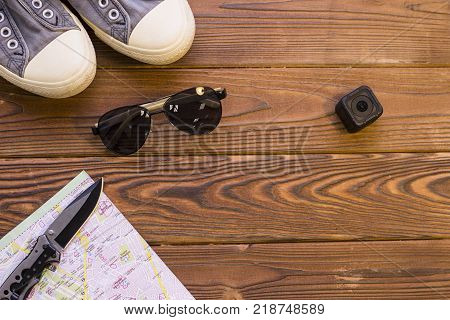 Man paking for a travel. Sport shoes, a swicthblade knife, sunglasses, an action camera and a folded map on a rustic wooden background. Space for a text or product display, top view.