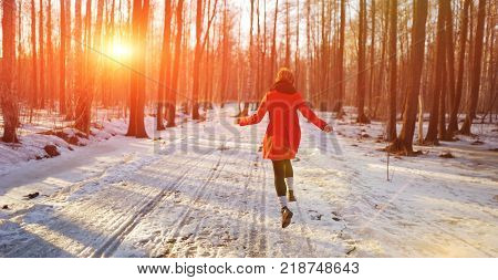 Young slender girl in a red coat runs along a snowy path in the Park, fun bouncing and waving his arms.